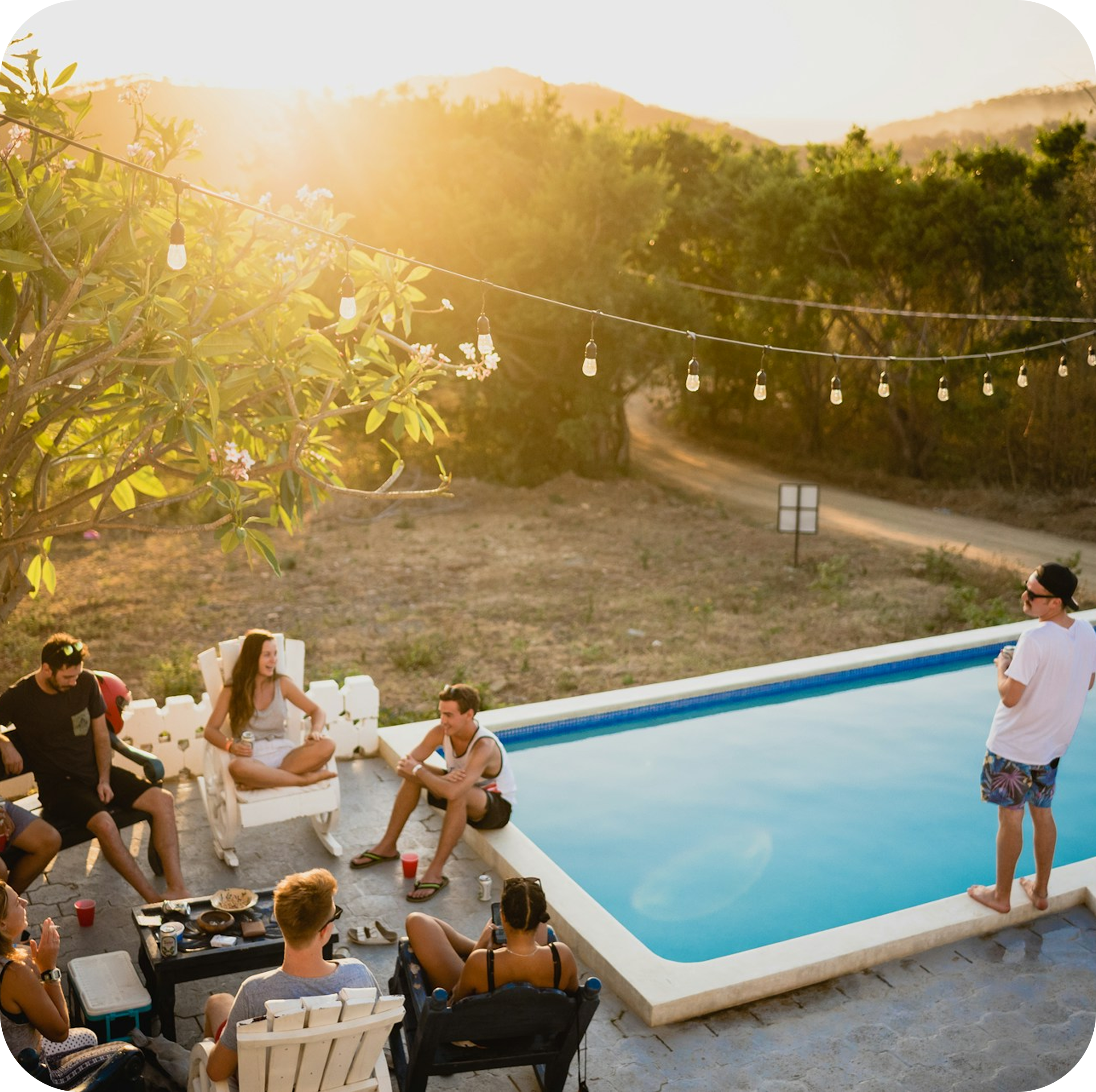 Group of people socialising by pool at golden hour with string lights